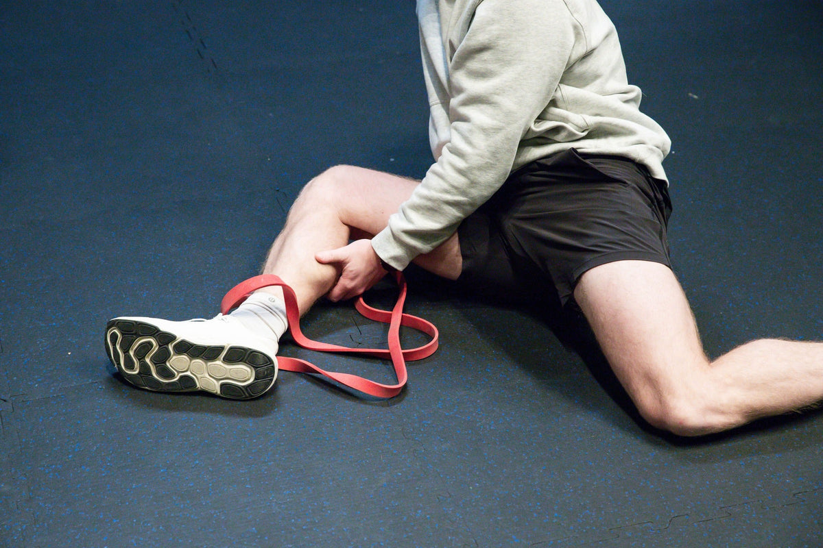 Athlete stretching on the gym floor using a resistance band around their ankle.