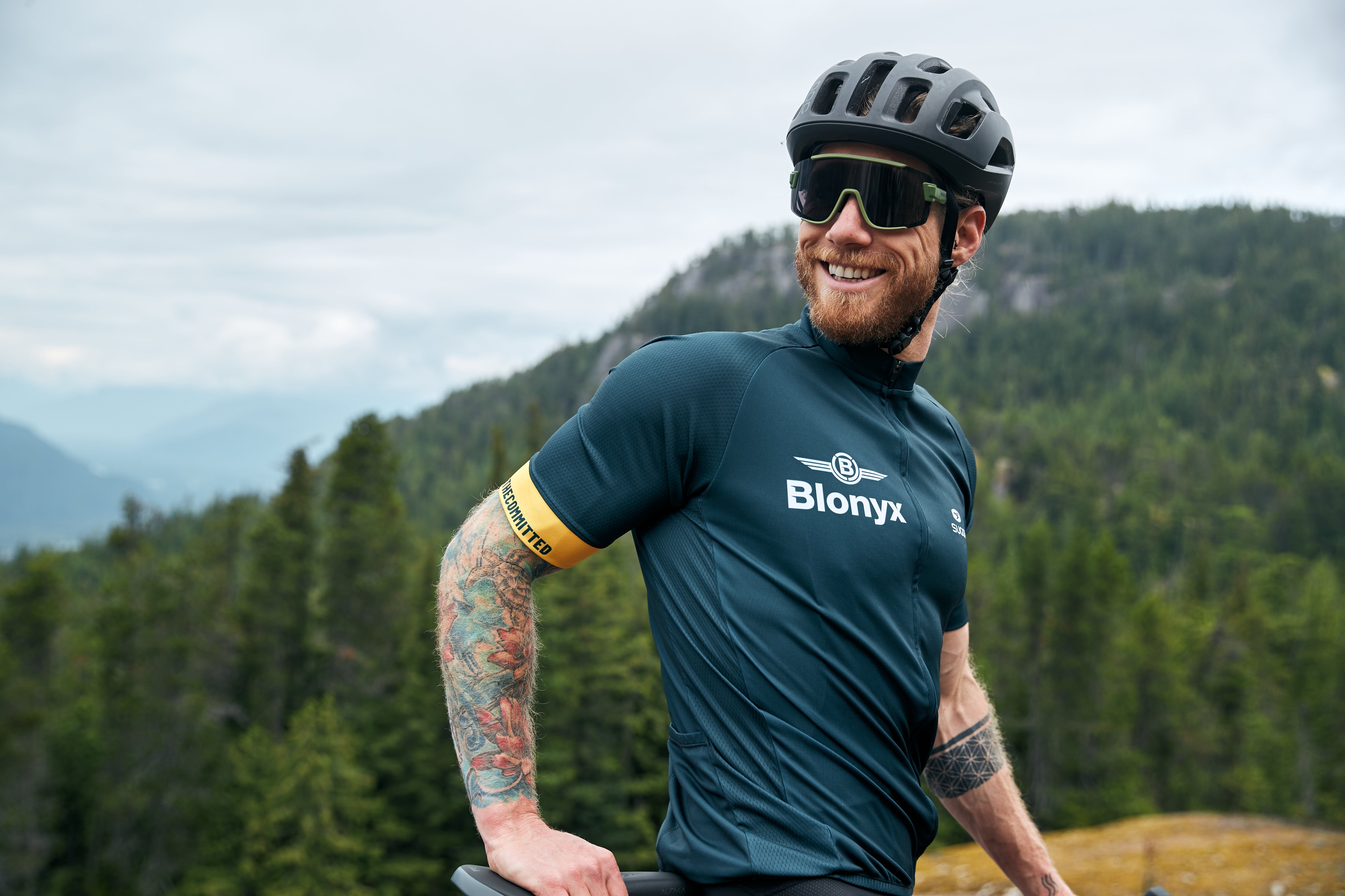 Cyclist smiling while resting at the top of a mountain trail.