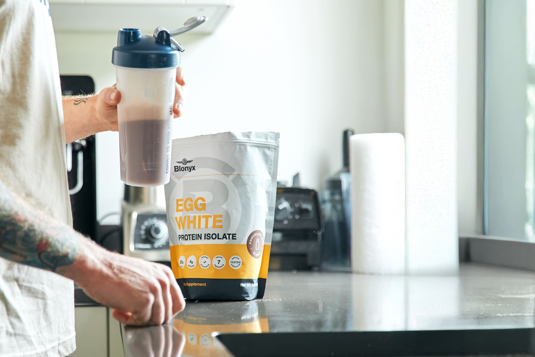 An Athlete in a Kitchen Holding A Shaker with Blonyx Egg White Protein