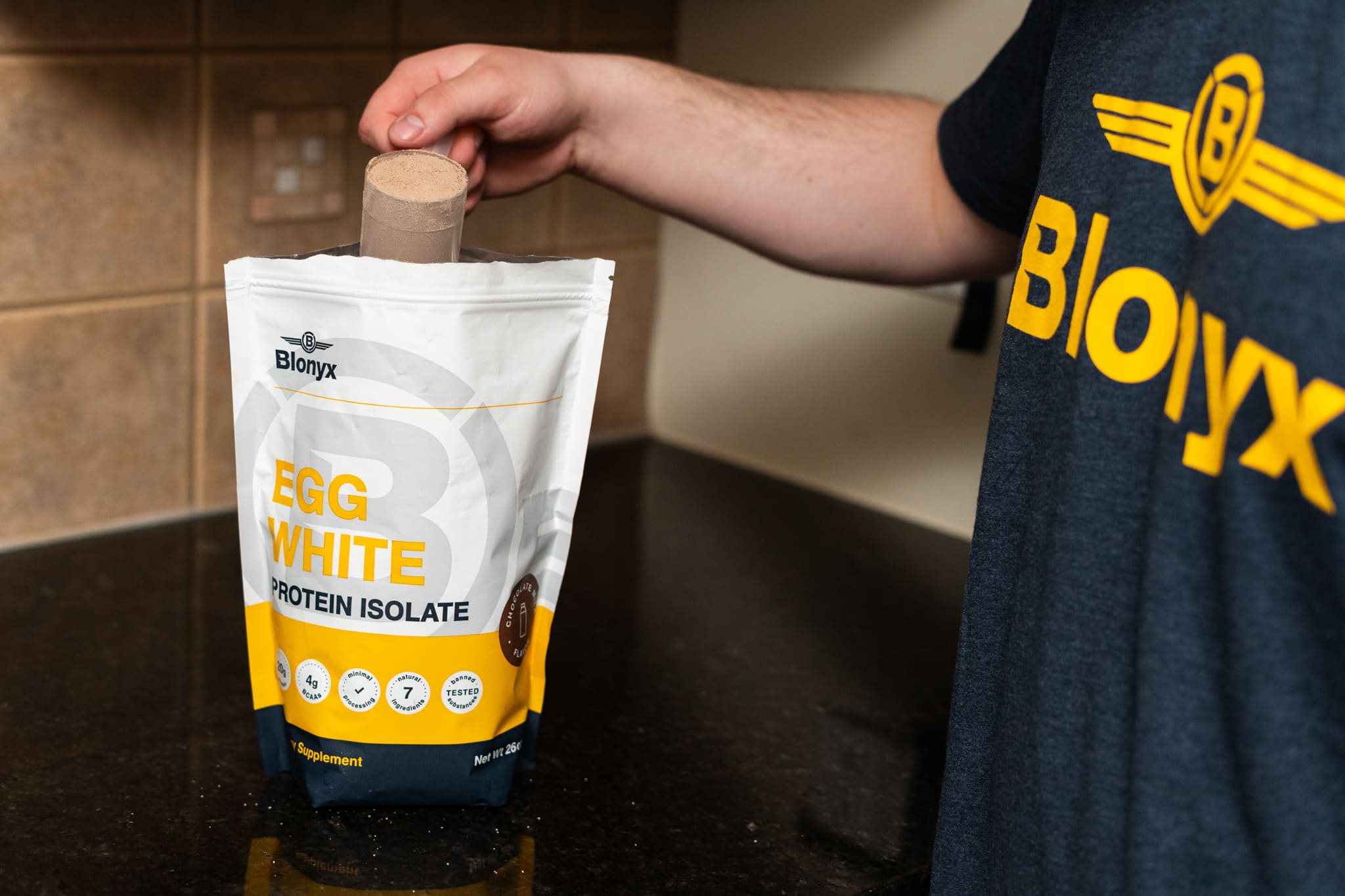 A person scoops Blonyx Egg White Protein Isolate powder from the pouch.