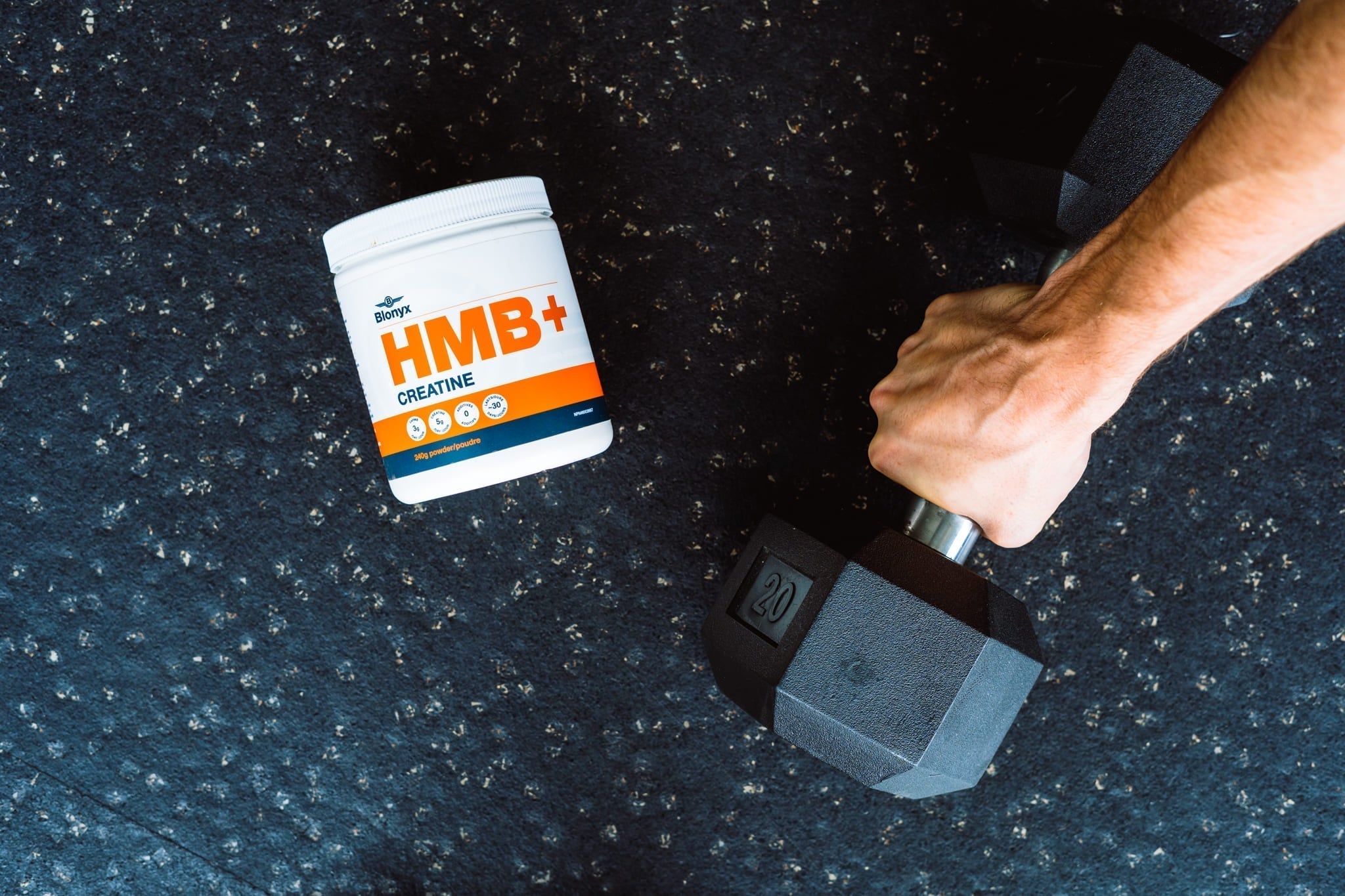 Blonyx HMB+ Creatine on a Gym Floor Next to Someone Picking up a Dumbbell