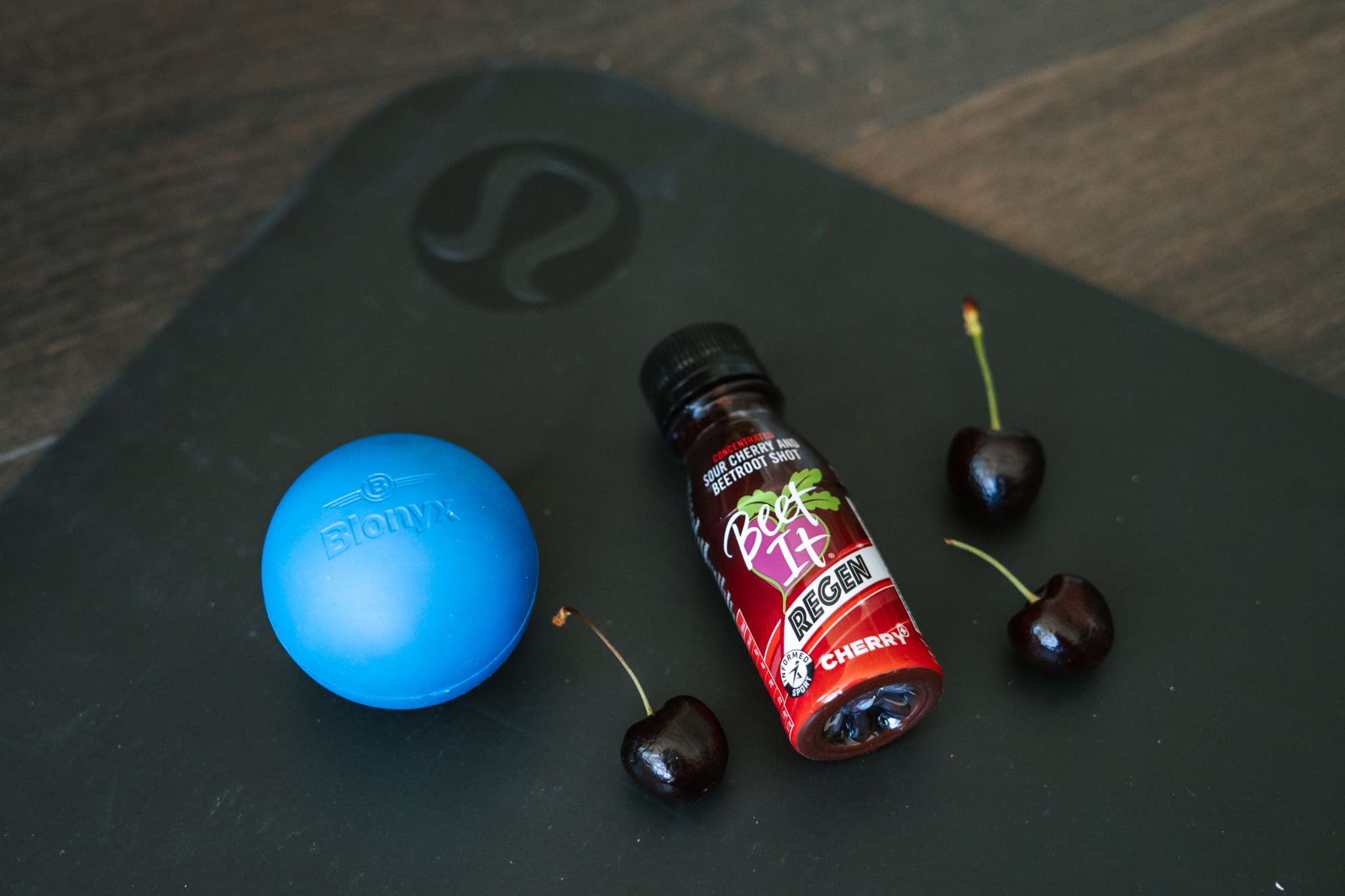 A Blonyx Lacrosse Ball, Beet It Regen Cherry+ Tart Cherry Juice Shot, and Cherries on a Yoga Mat