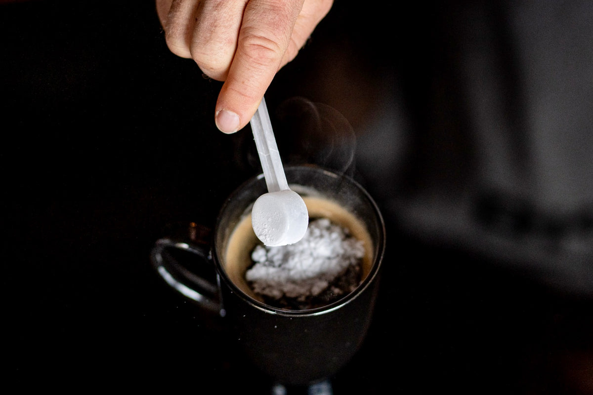 Someone adding a scoop of creatine to a cup of coffee