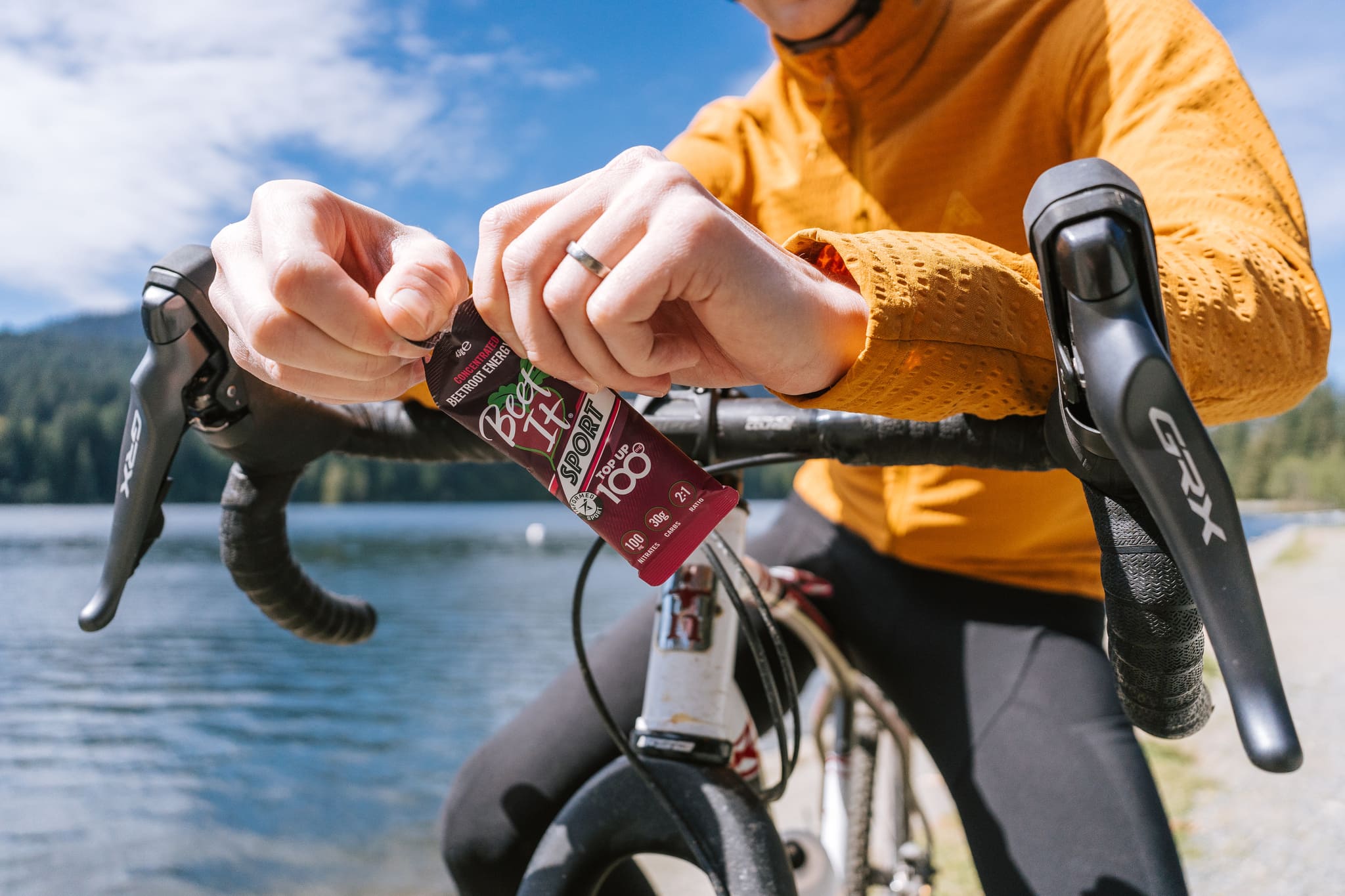 Gravel cyclist sitting on a bike opening a Beet It Sport Top Up 100 gel