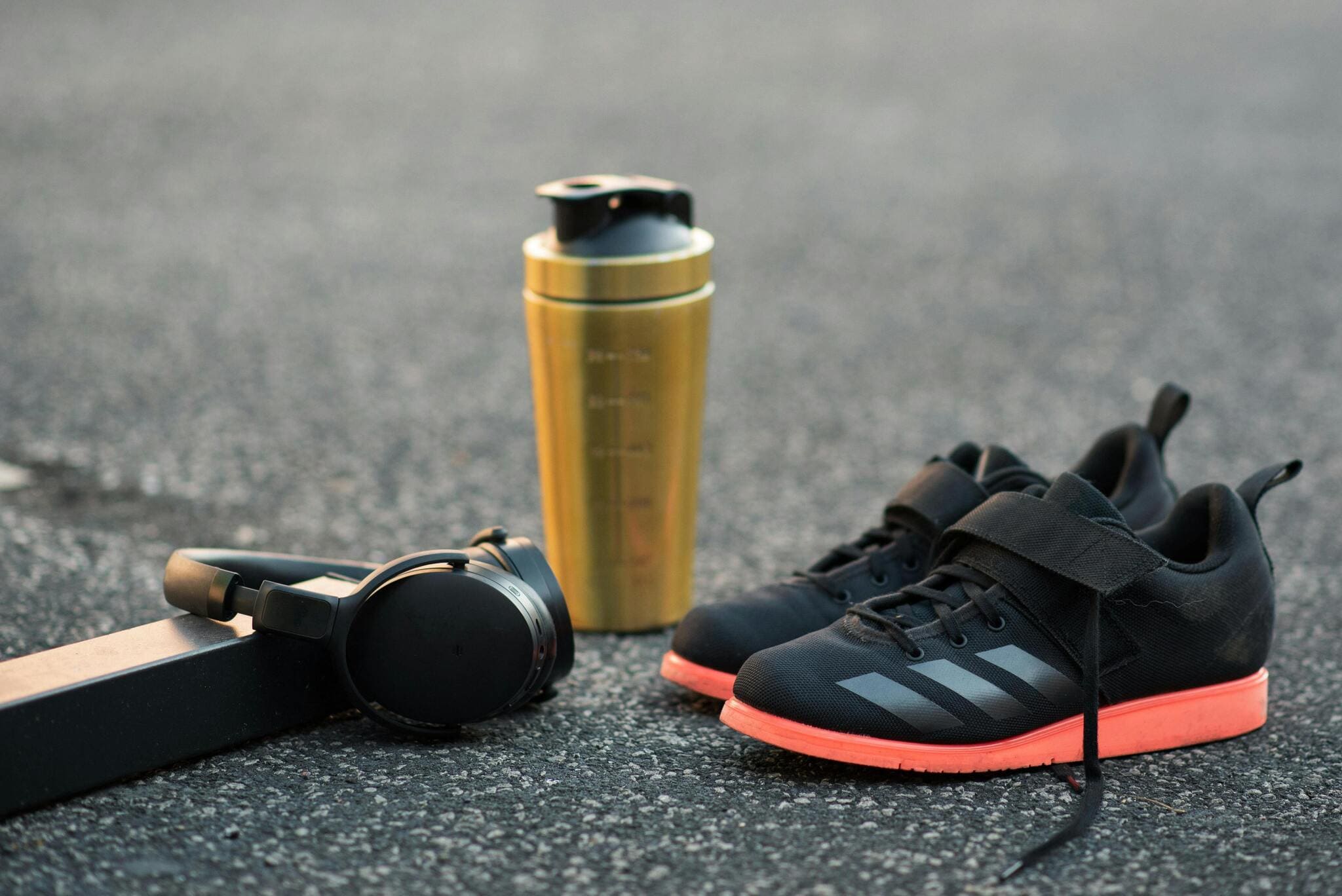 A travel mug, headphones, and sneakers on asphalt.