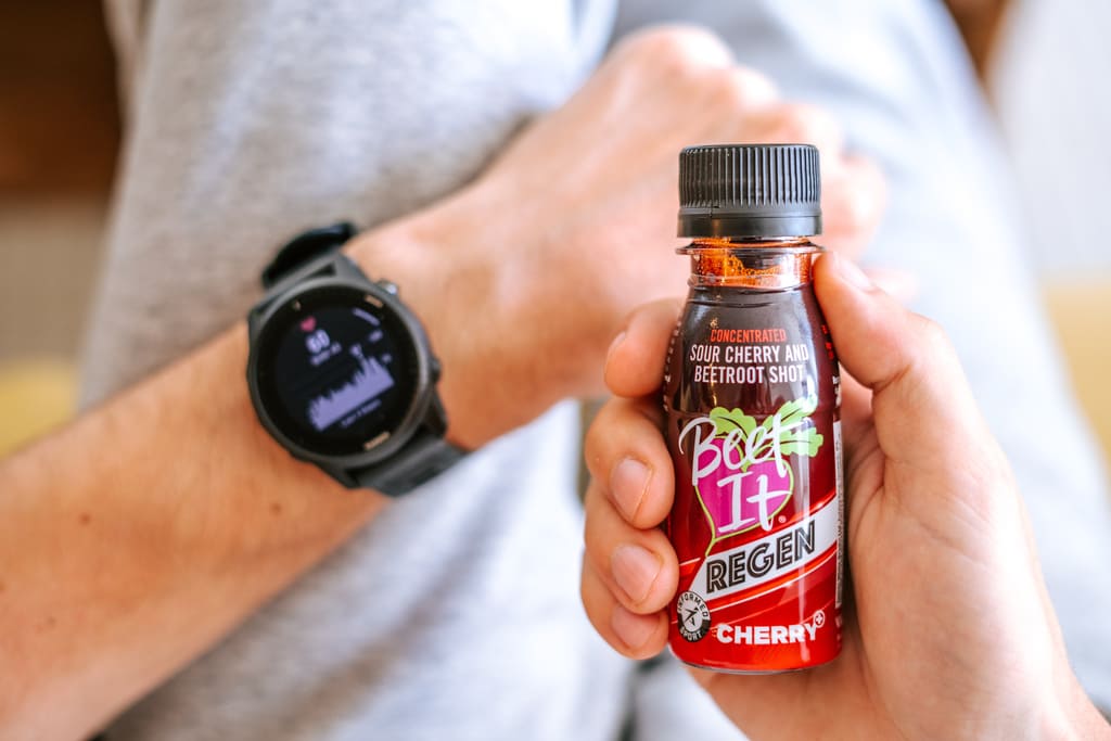 Person holding a bottle of Beef Regen Cherry flavor supplement with a smartwatch in the background.