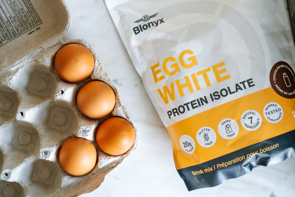 Egg carton with eggs and a package of Blonyx Egg White Protein Isolate on a white surface.