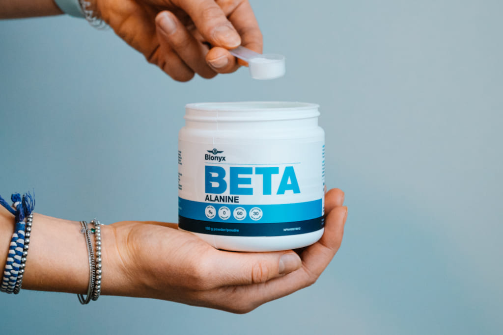 Blonyx Beta Alanine powder supplement being scooped from container, providing 6g daily beta-alanine to support muscle endurance, delay fatigue, and improve athletic performance.