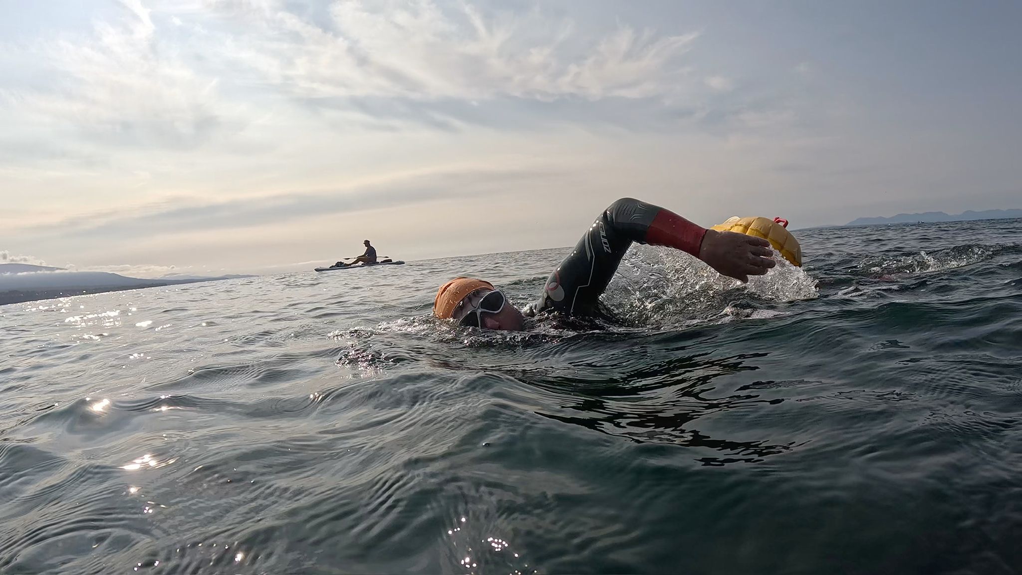 Person swimming in open water with a yellow swim cap and goggles.