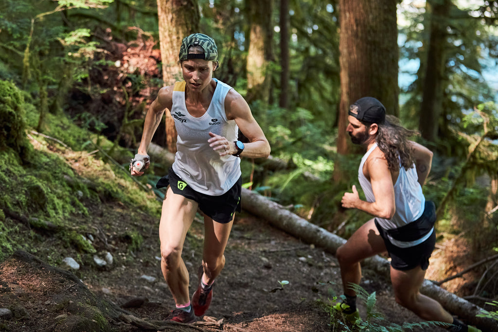 Trail runners climbing a steep forest trail during endurance training with Beet It Sport nitrate energy gel for sustained performance.