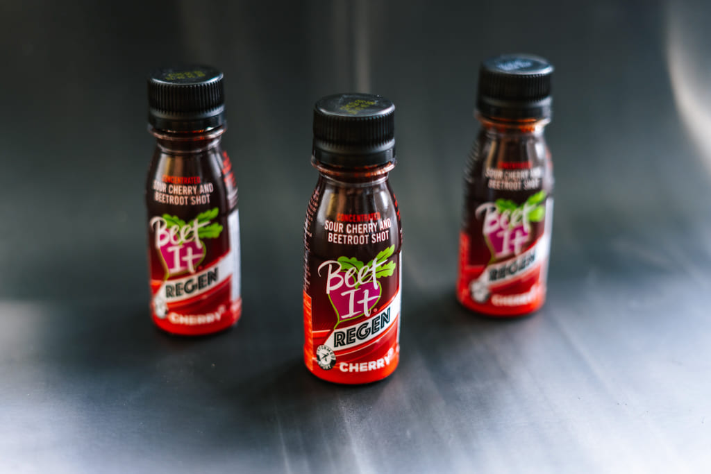 Three bottles of Beet It Regen Cherry+ tart cherry and beetroot recovery shots on a table, sports nutrition for athletic recovery and reduced muscle soreness.