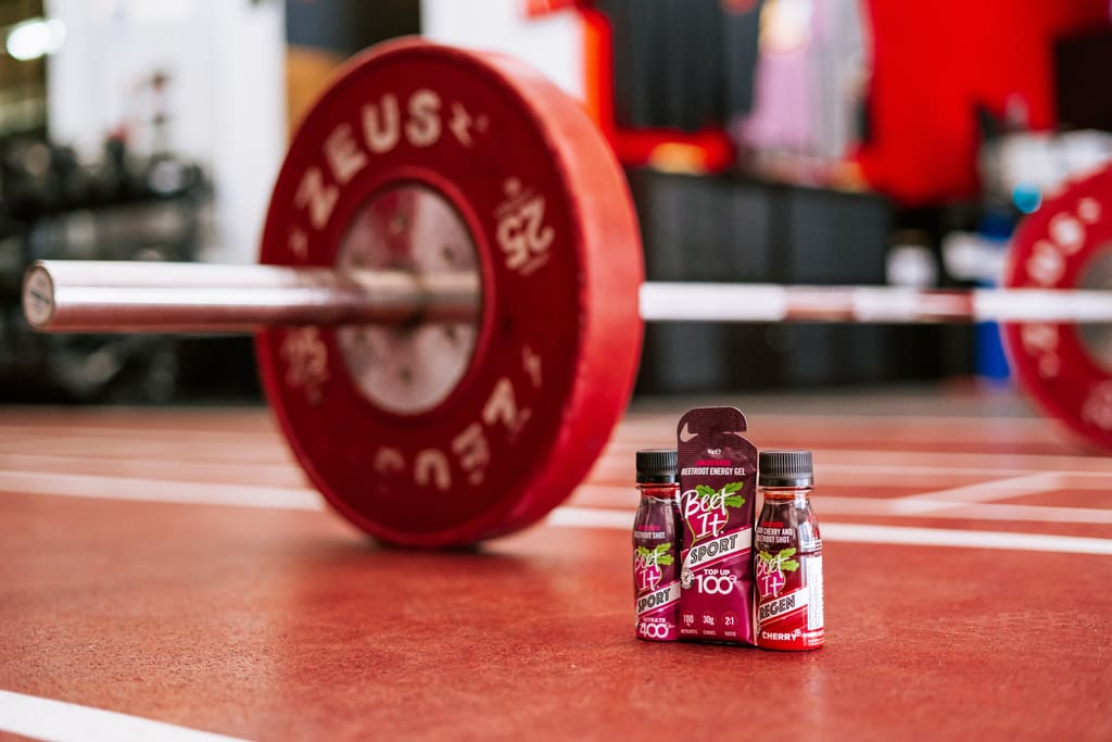 Beet It Sport Nitrate 400, Top Up 100, and Regen Cherry+ in Front of a Barbell