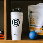 White shaker bottle with Blonyx logo next to a protein powder package and blue ball on a wooden shelf.
