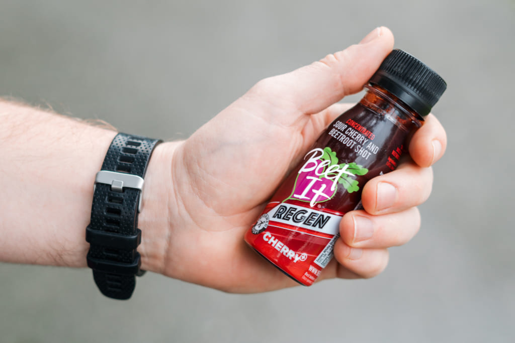 Close-up of a hand holding a Beet It Regen Cherry+ tart cherry and beetroot shot, a recovery supplement for athletes and active individuals.