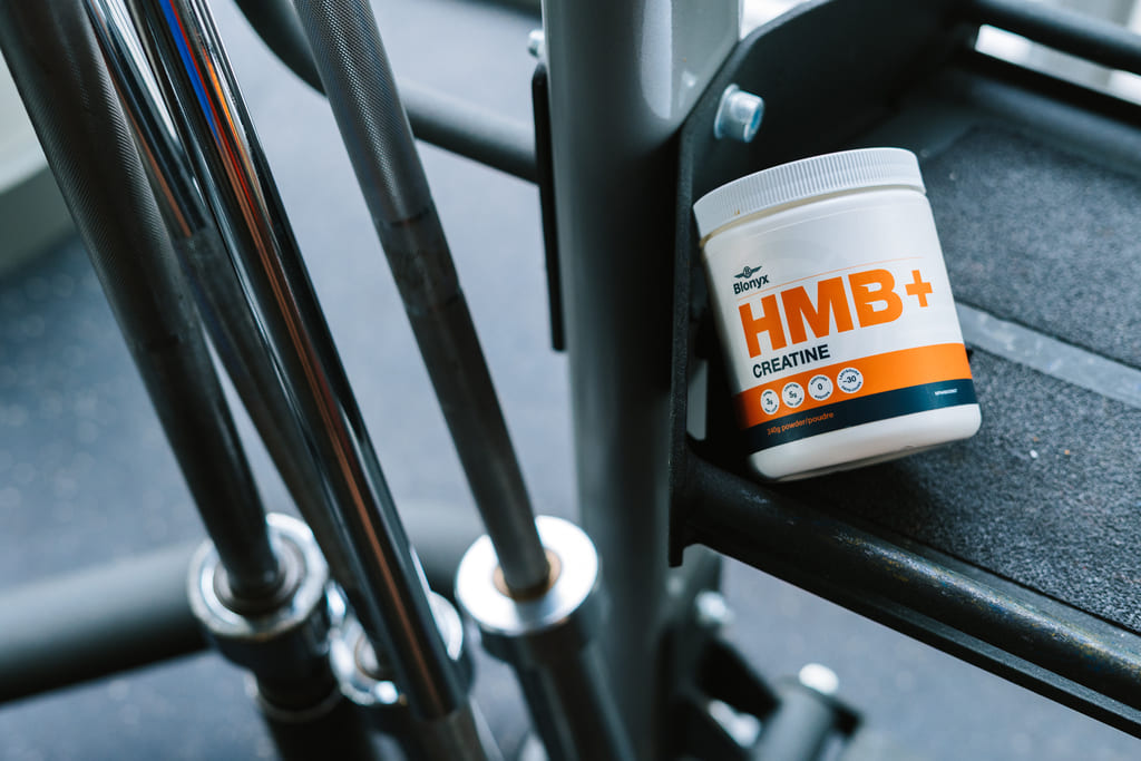 Blonyx HMB+ Creatine supplement container beside gym equipment and barbells in strength training facility
