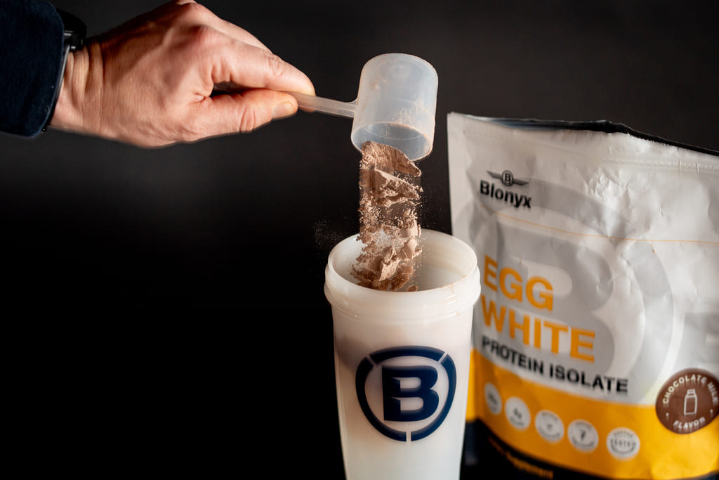 A person adding a scoop of Blonyx Egg White Protein Isolate to a shaker.