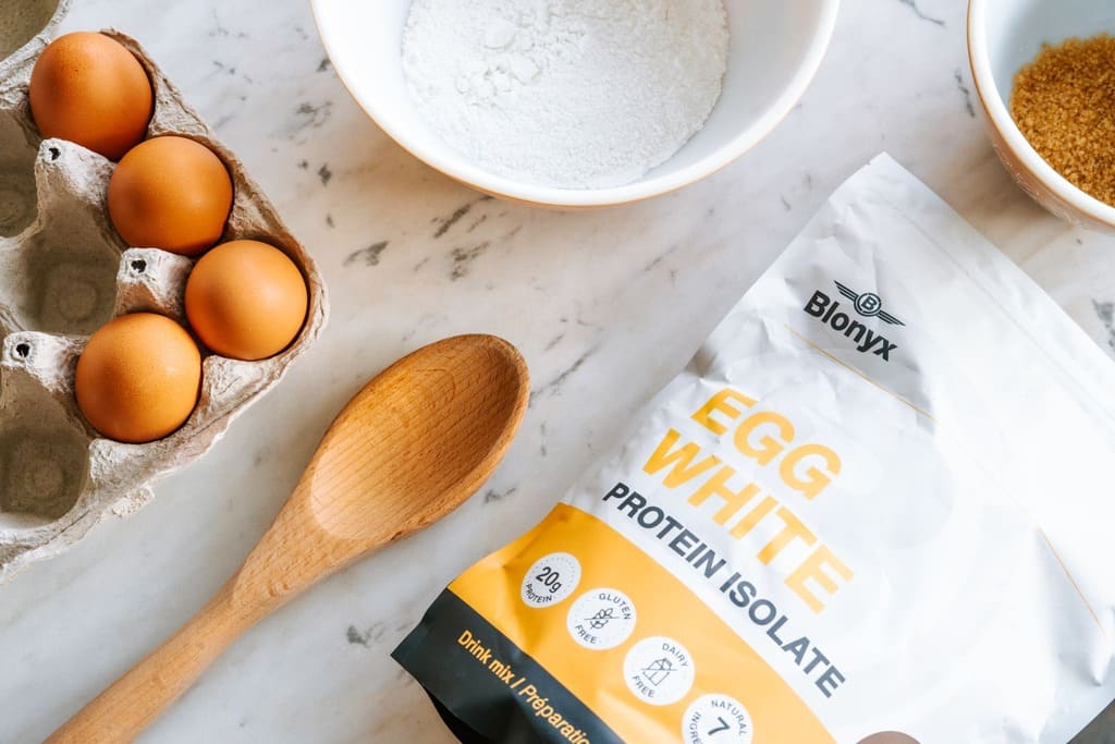 Table of baking ingredients including a bag of Blonyx Egg White Protein Isolate, eggs, flower, and sugar