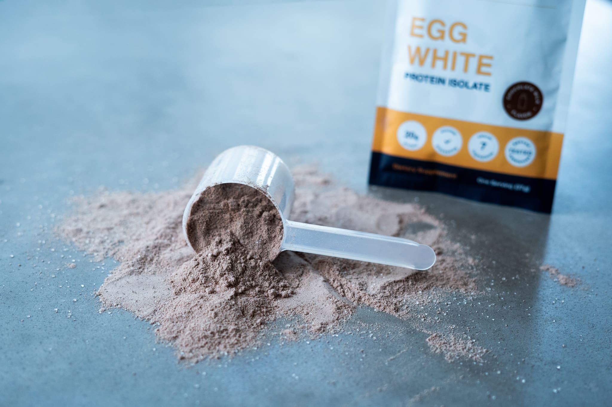 A Scoop of Egg White Protein Powder Spills onto a Concrete Table