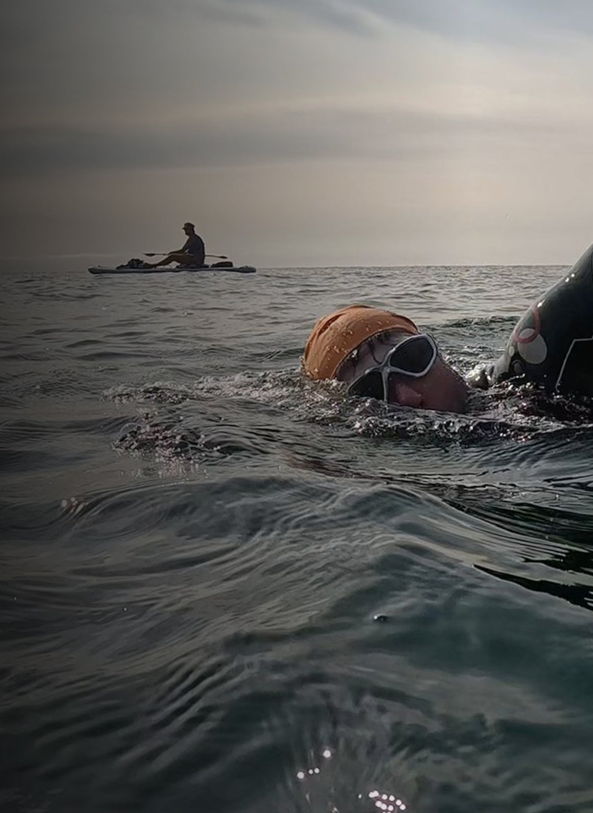Person swimming in open water with another person in a kayak in the distance.