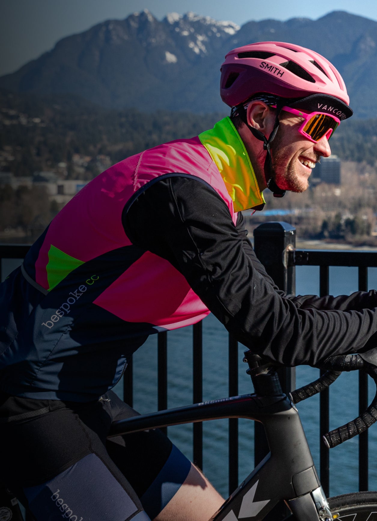 A cyclist wearing pink and yellow kit and looking out at the mountains across the water