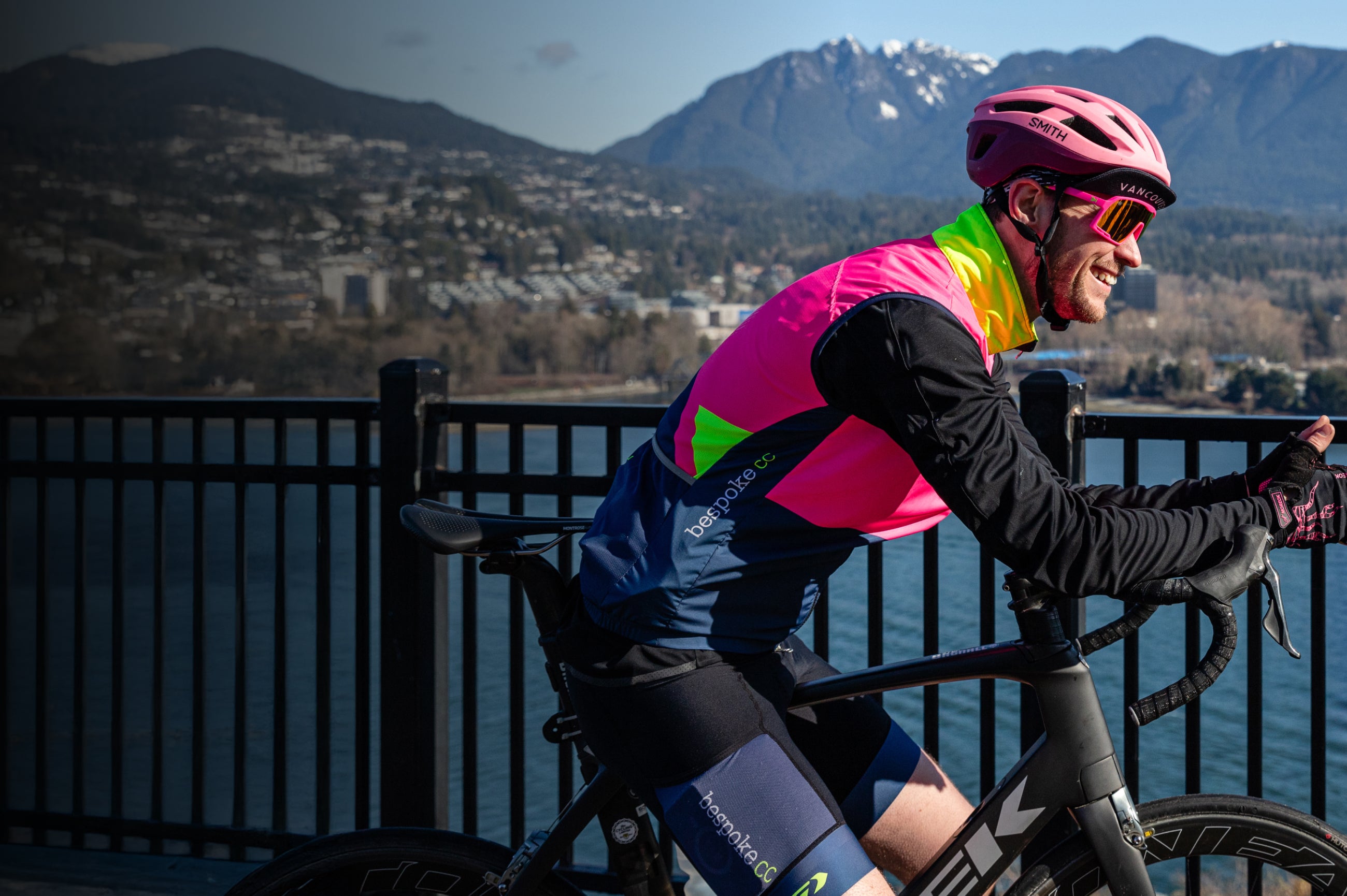 A cyclist wearing pink and yellow kit and looking out at the mountains across the water