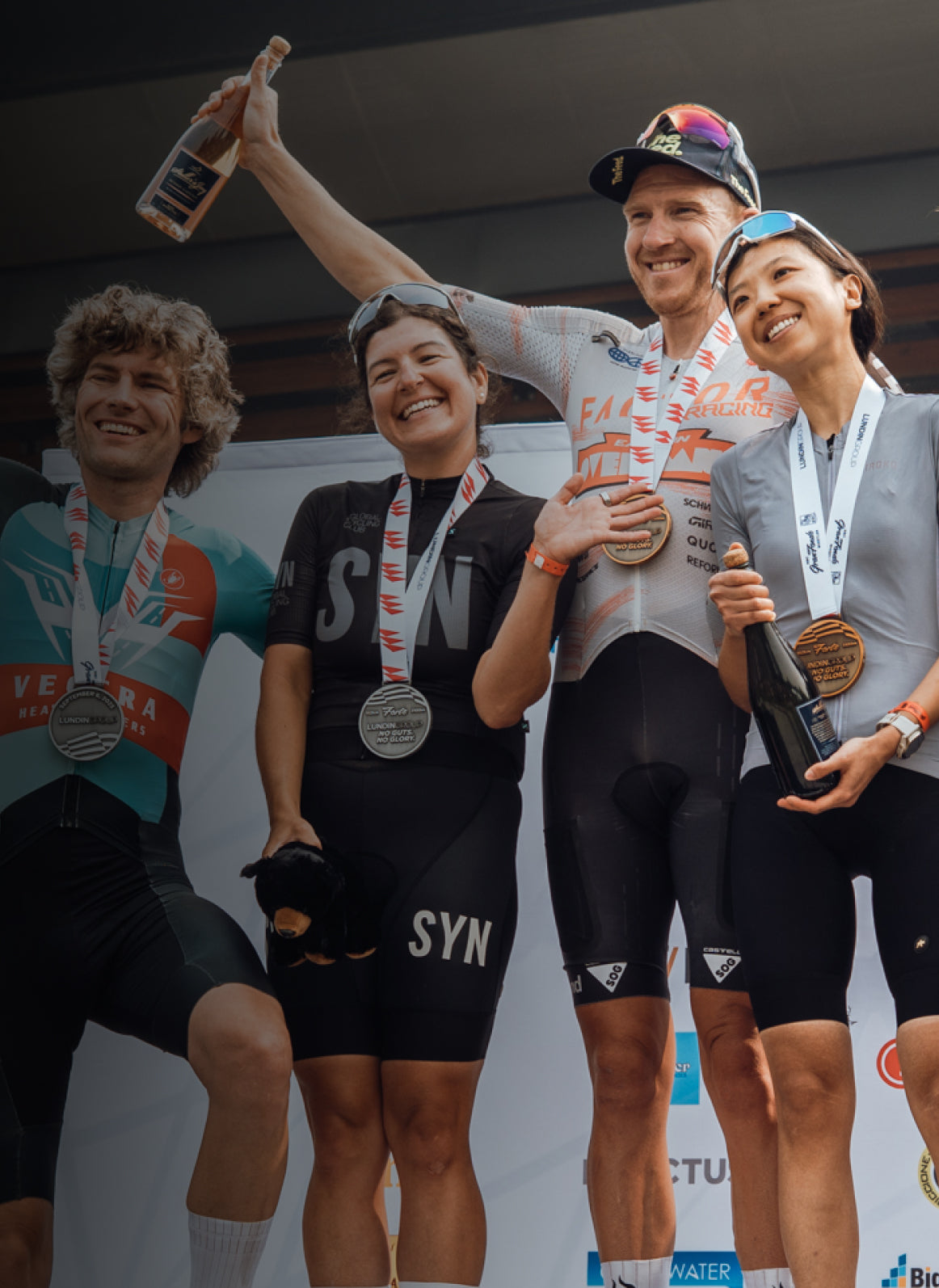 Four athletes celebrating with medals and bottles on a podium