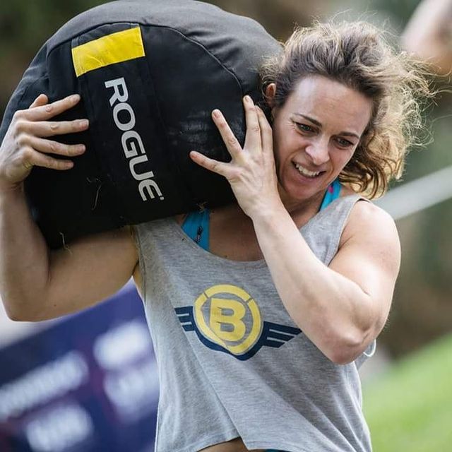 Female athlete carrying a Rogue sandbag over her shoulder during a functional fitness competition.