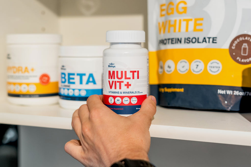 Hand reaching for Blonyx Multivit+ daily multivitamin with Hydra+, Beta Alanine, and Egg White Protein Isolate on a supplement shelf.