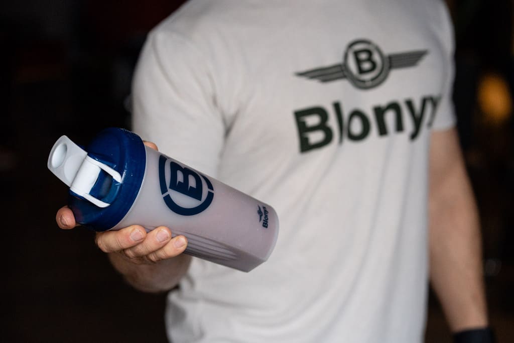 Hand holding a shaker cup against a black background with Blonyx Egg White Protein Isolate inside