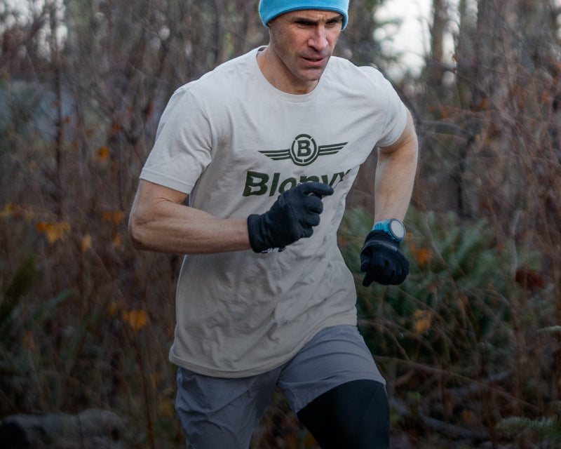 Man running outdoors in a forest wearing a blue beanie and grey t-shirt with a Blonyx logo.