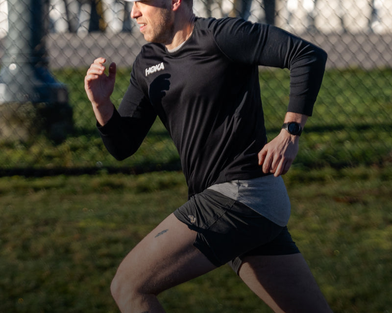 Man running outdoors on a grassy area with a fence in the background