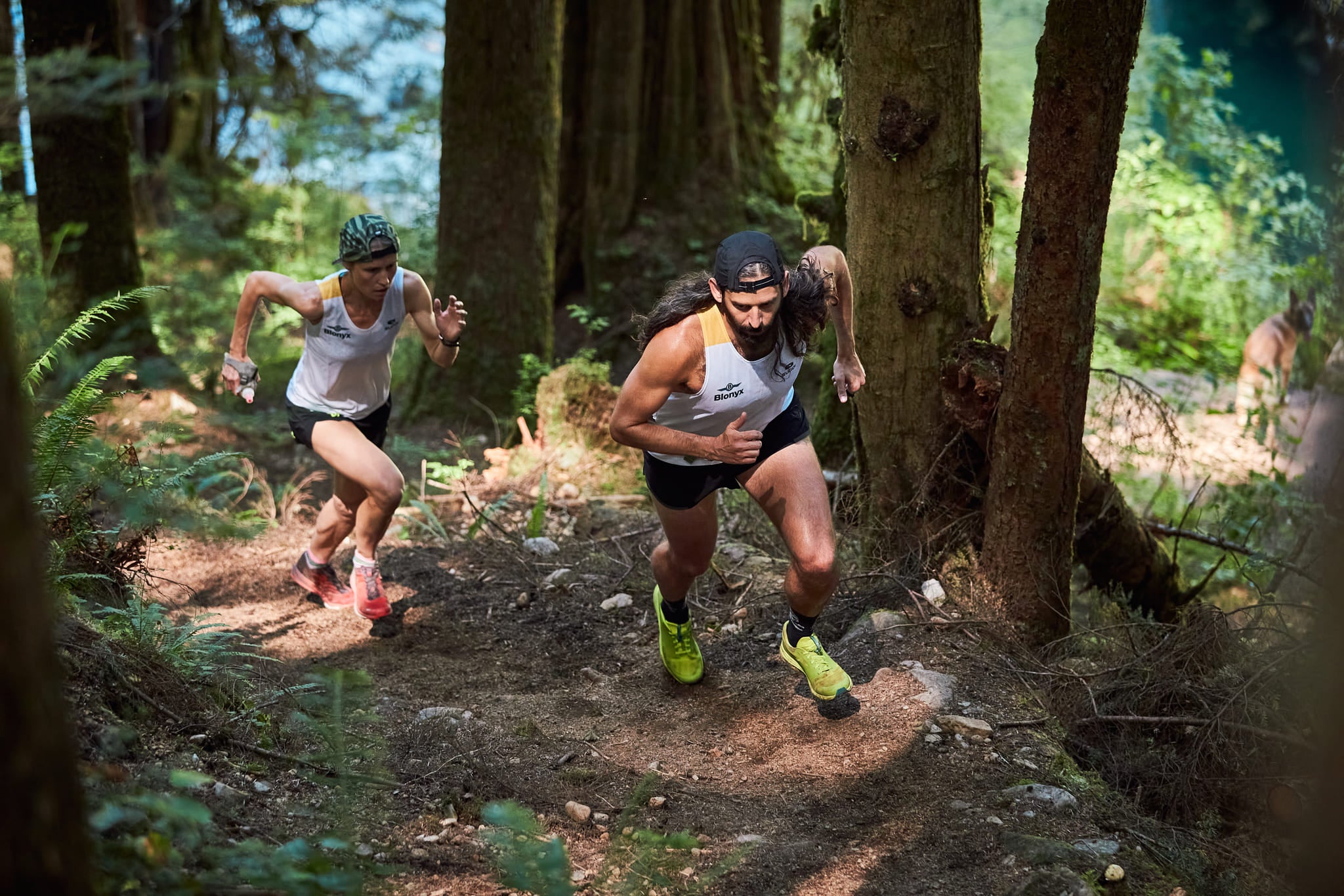 A Male and Female Trail Runner Wearing Blonyx Singlets Running Up a Trail