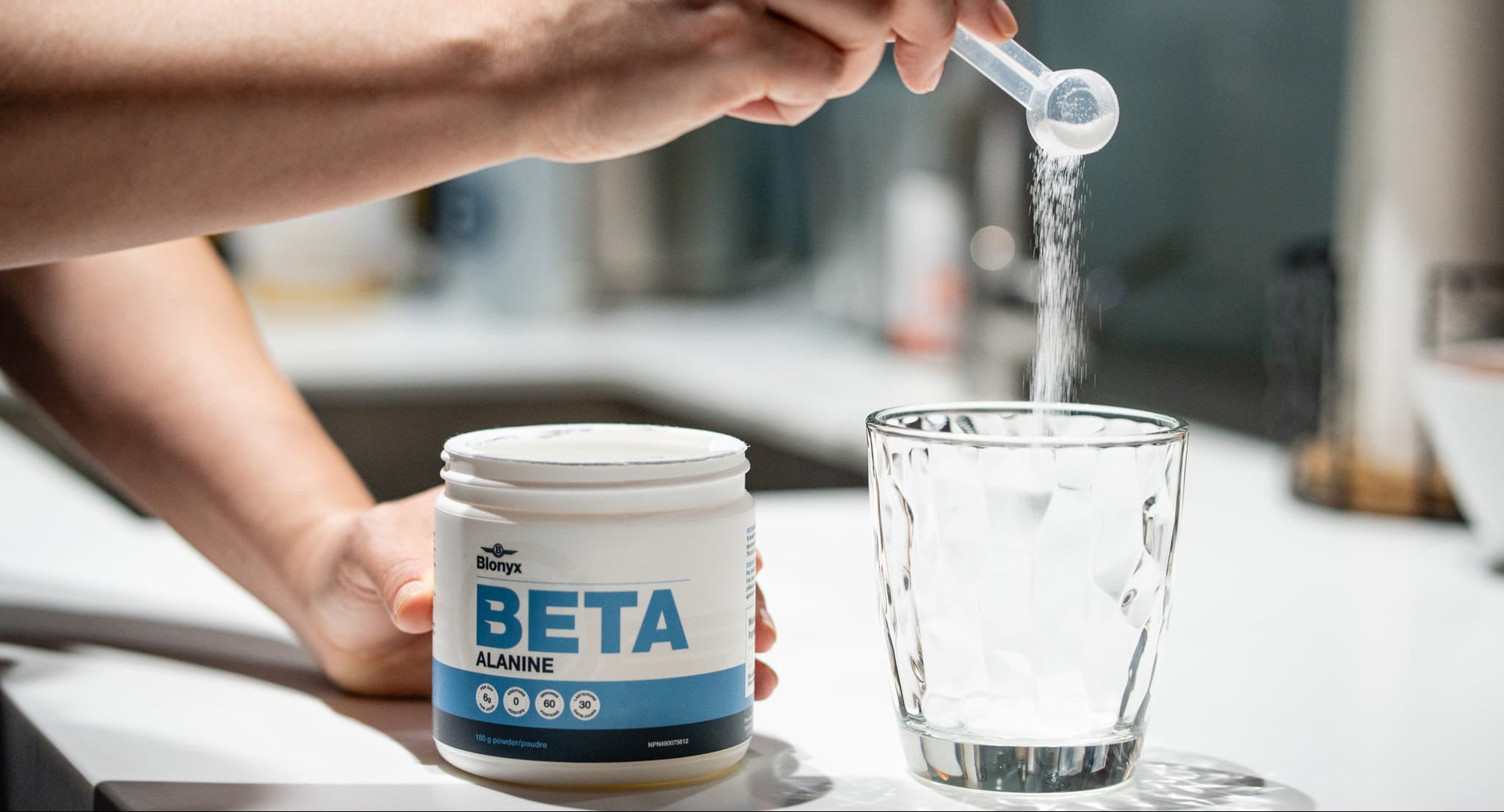 A person adding a scoop of Blonyx Beta Alanine to a glass.