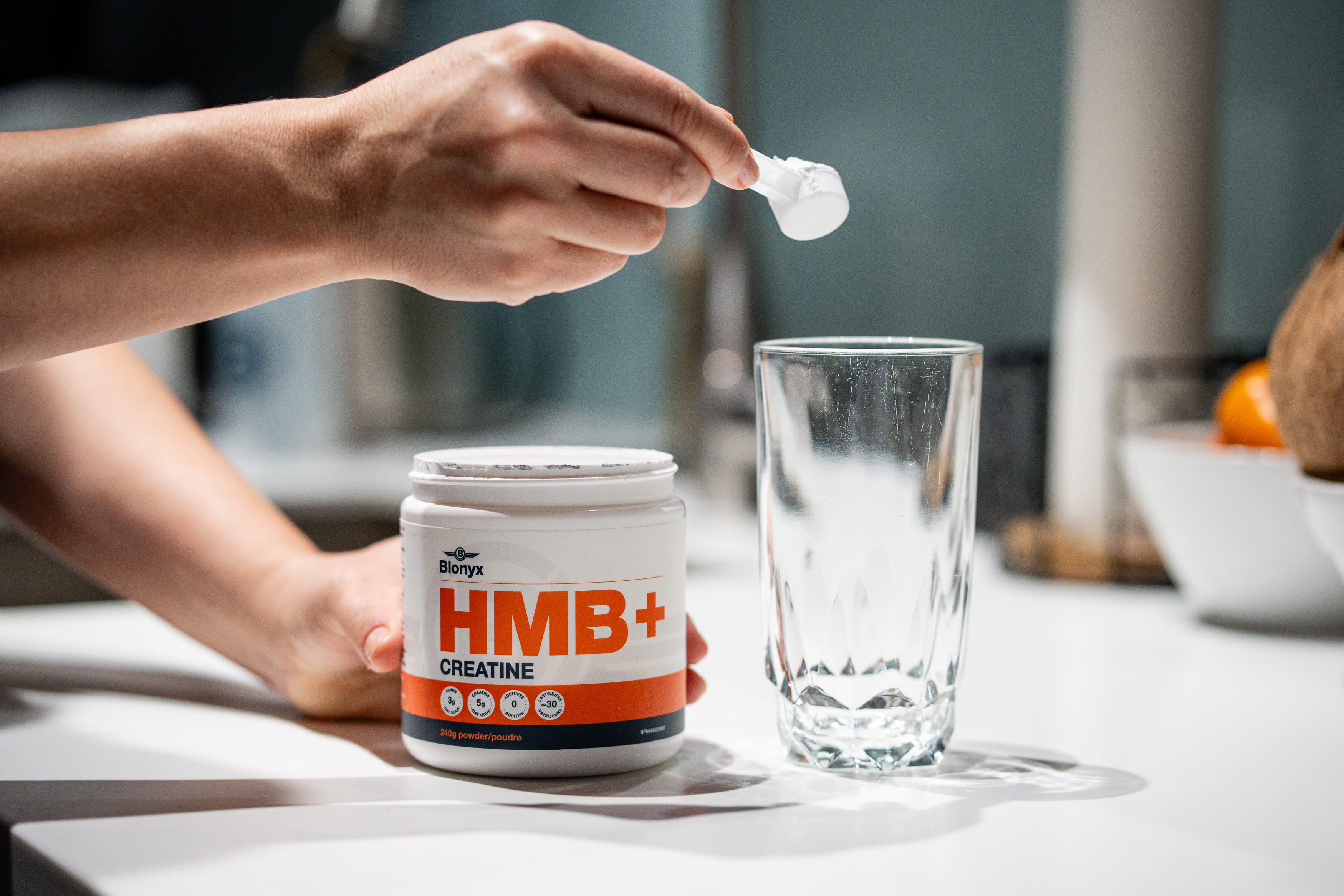A person adding a scoop of Blonyx HMB+ Creatine to a glass.