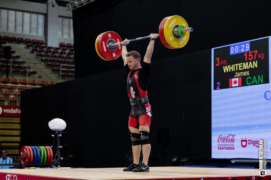 Weightlifter lifting a barbell with colorful weights in a competition setting.
